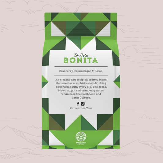 A Mucaro Coffees stand-up coffee bag with a green and white geometric pattern, featuring the brand name 'La Isla BONITA' on the front label. The bag is centered against a pale pink background with faint hand-drawn mountain silhouettes.