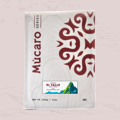A package of Mucaro Series El Valle coffee from Colombia, shown against a light pink background with subtle topographic line drawings. The package is white with a large dark red Aztec-style graphic on the right, vertical 'Mucaro Series' branding on the left, and the 'El Valle' label near the bottom.
