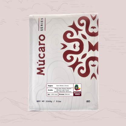 A package of Mucaro Series coffee from Ethiopia Gera, shown against a light pink background with faint mountain illustrations. The packaging is white with a dark red traditional pattern and text.