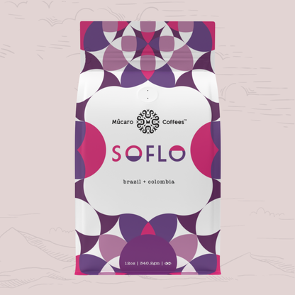 A 12oz bag of Múcaro Coffees Soflo Blend from Colombia and Brazil, featuring a modern geometric pattern in purple, magenta, and white on a light pink background.
