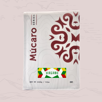A package of Mucaro Series Yirgamo coffee blend, featuring a white bag with a dark red stylized graphic and a colorful label at the bottom, set against a pale pink background with faint topographical line drawings.